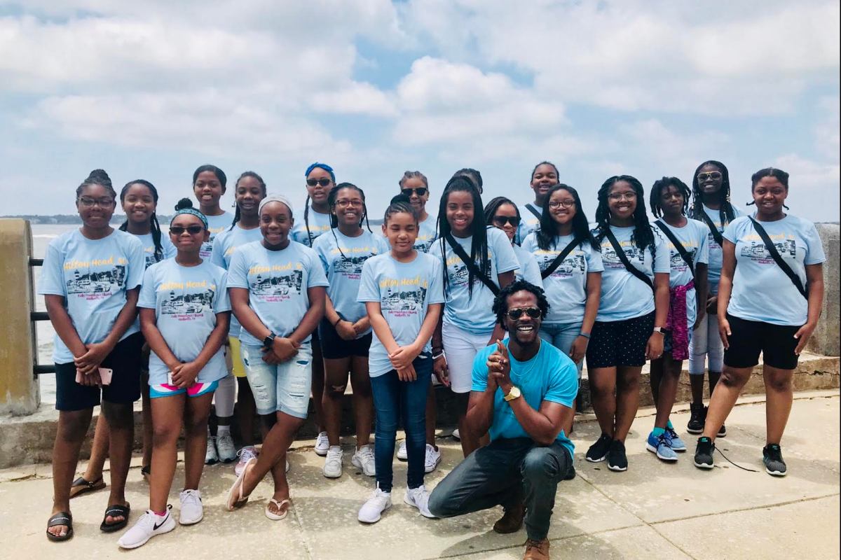 Black students and CHIEF GODFREY KHILL gathered outdoors during a Gullah Geechee educational experience