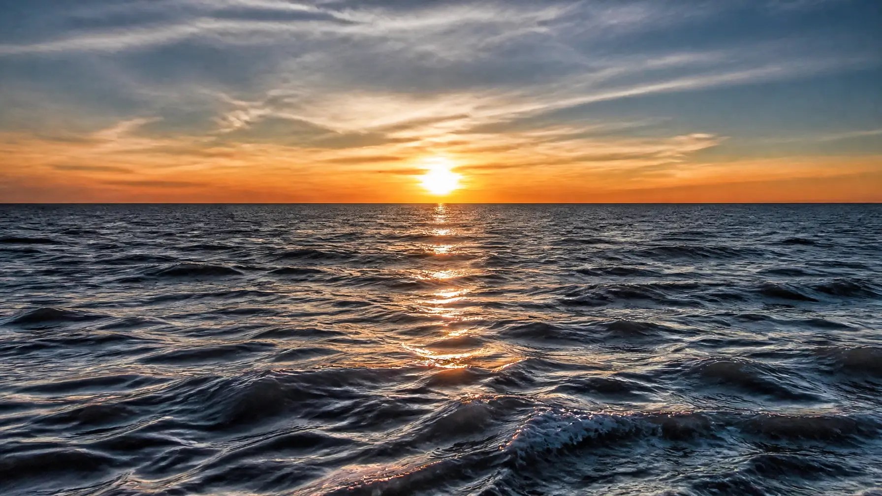 Sunset over a calm ocean with vibrant sky hues.