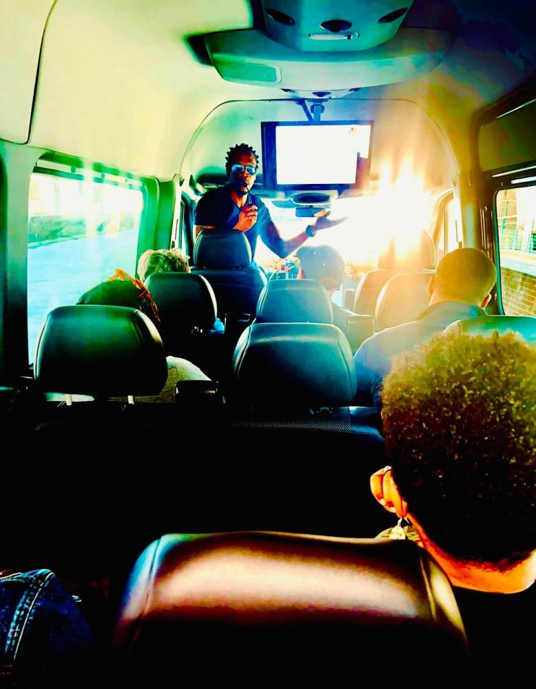 Person speaking to passengers inside a brightly lit bus.